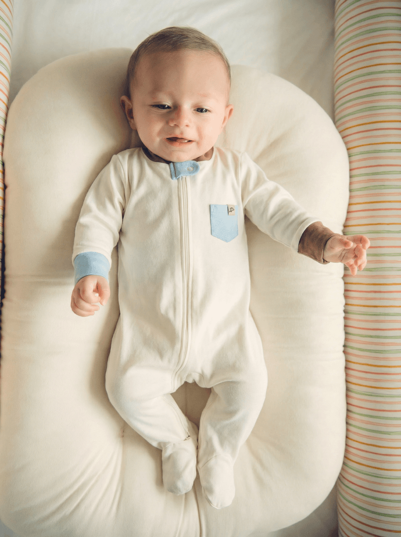 Bebê sorrindo vestindo o Macacão de Zíper off-white com detalhes azul e marrom